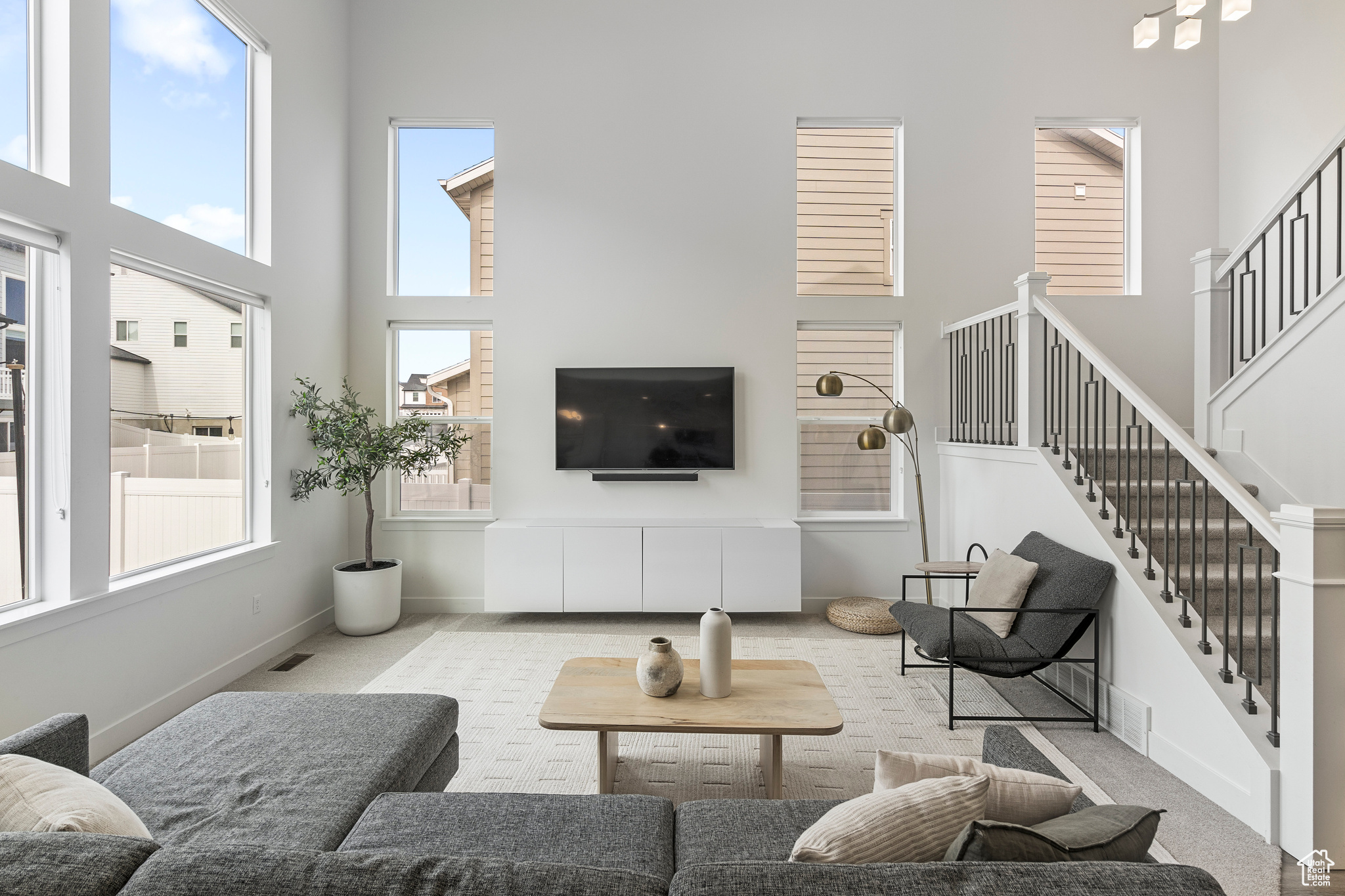 Carpeted living room featuring stairway, a high ceiling, baseboards, and a wealth of natural light