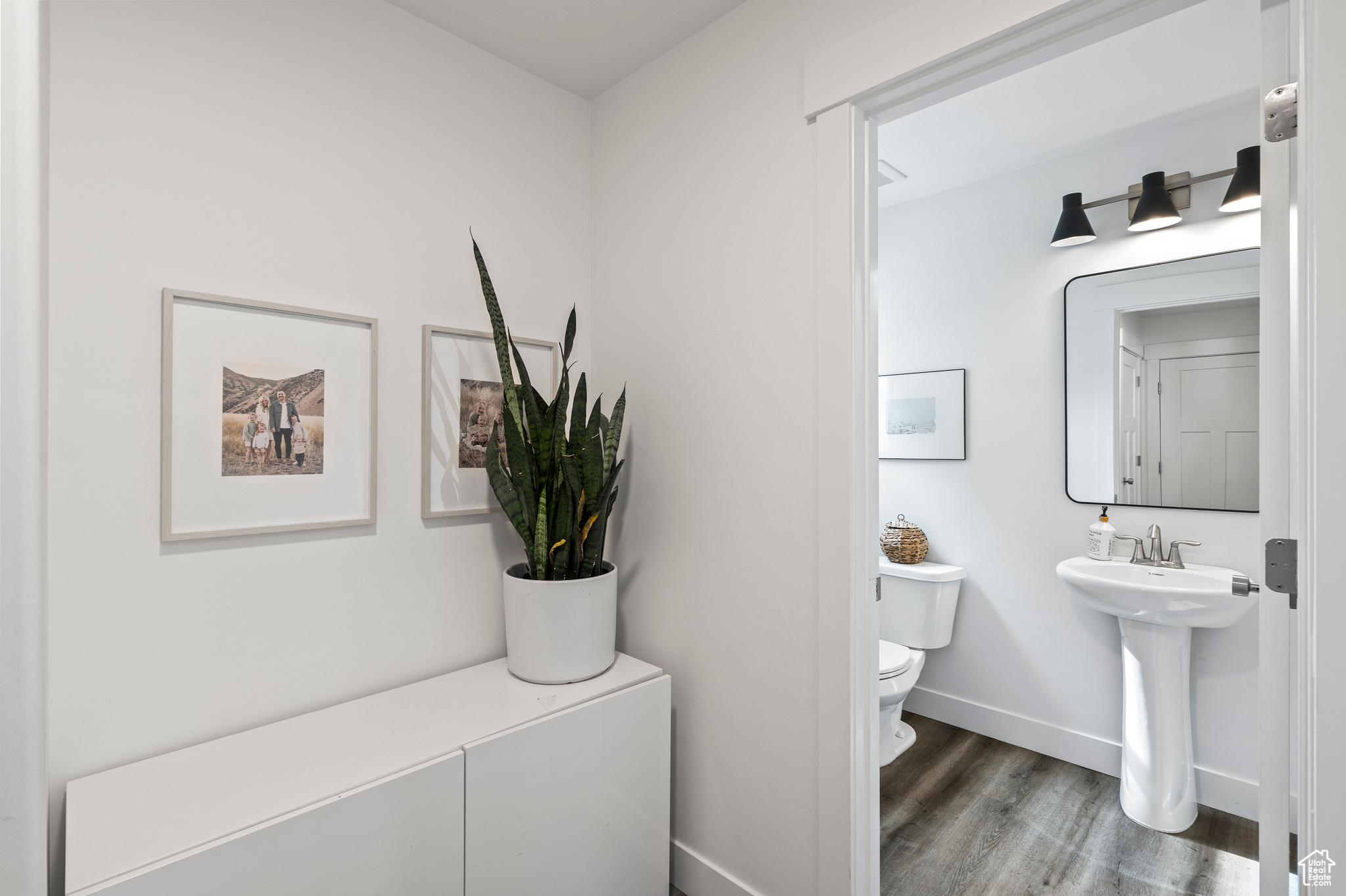Half bath with toilet, wood finished floors, baseboards, and a sink