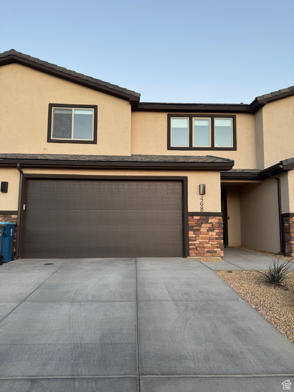 Multi unit property with stucco siding, stone siding, a garage, and driveway