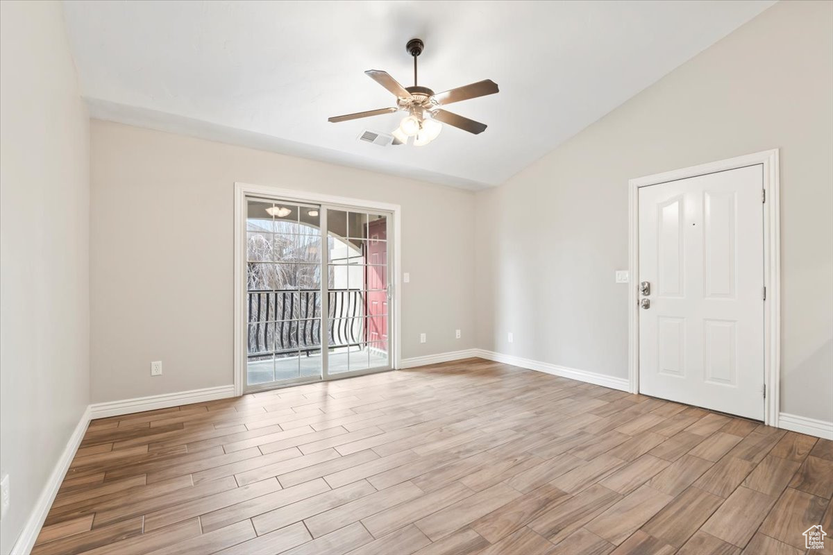Spare room with wood finished floors, baseboards, visible vents, ceiling fan, and vaulted ceiling
