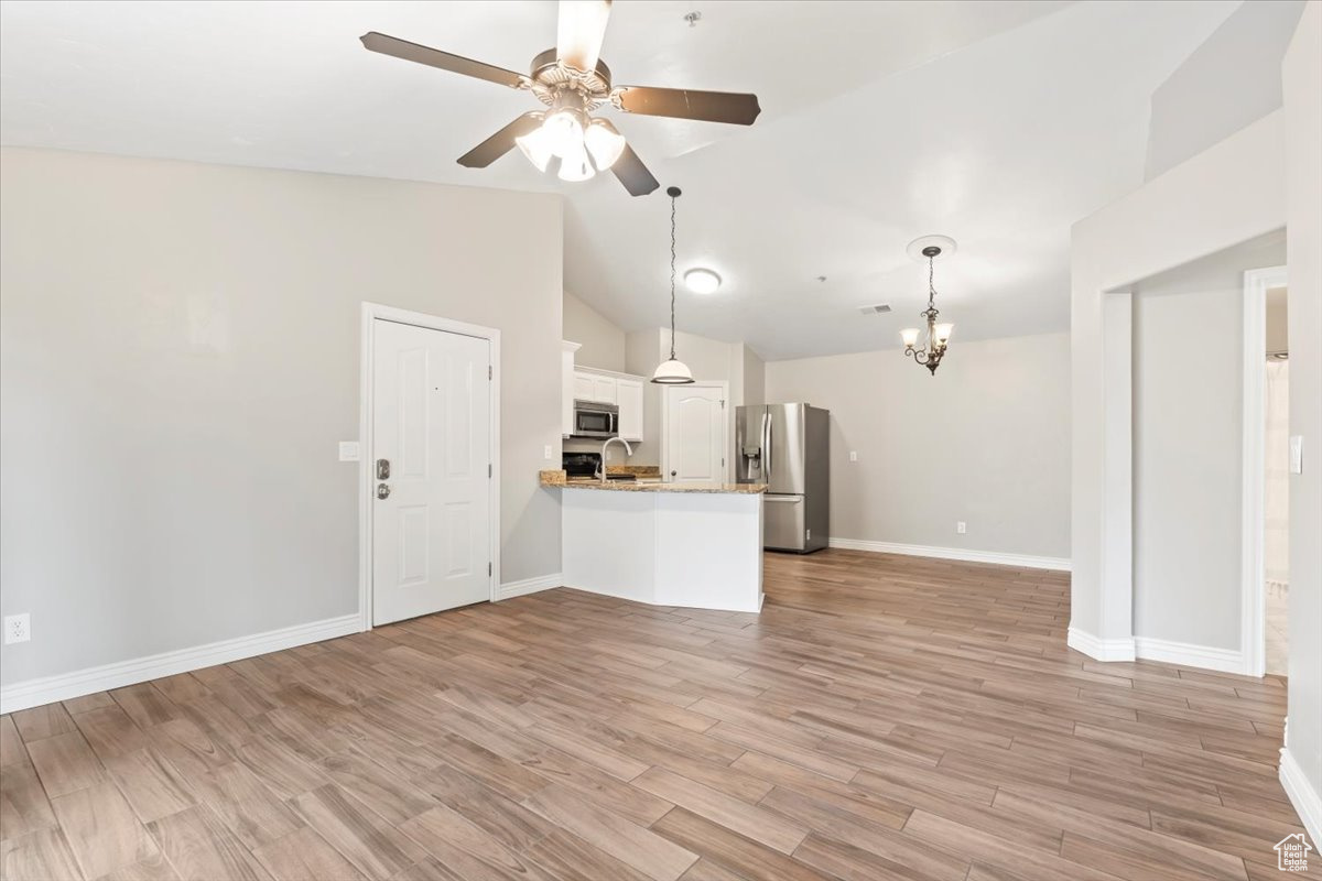 Unfurnished living room with light wood-style flooring, ceiling fan with notable chandelier, baseboards, and vaulted ceiling