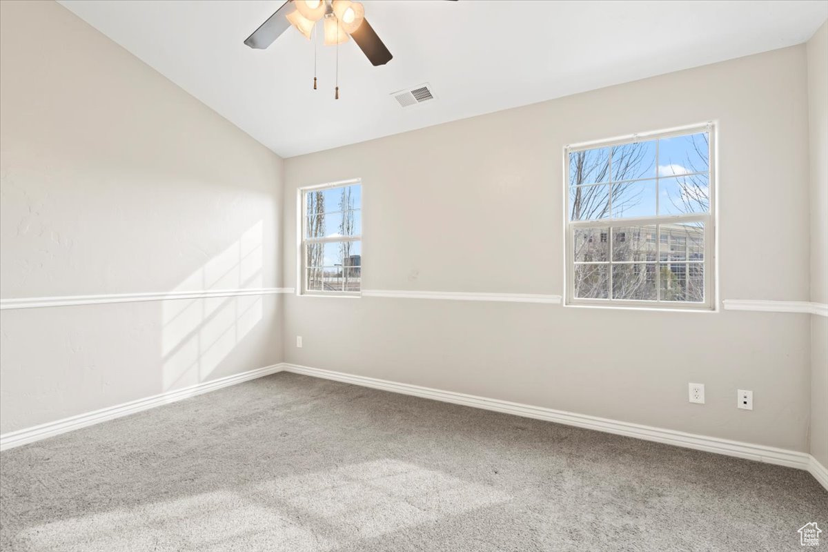 Spare room with visible vents, a ceiling fan, carpet flooring, baseboards, and vaulted ceiling
