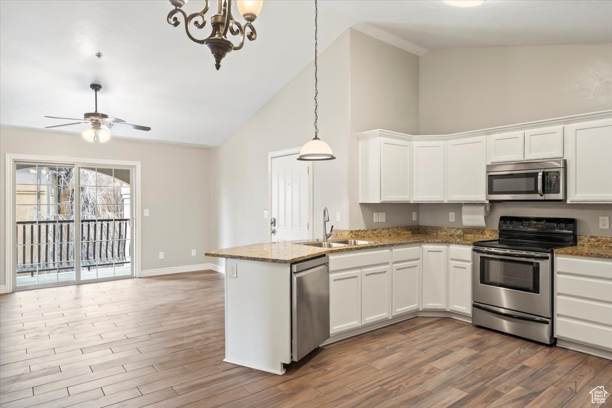 Kitchen with a sink, wood finished floors, appliances with stainless steel finishes, a peninsula, and white cabinets