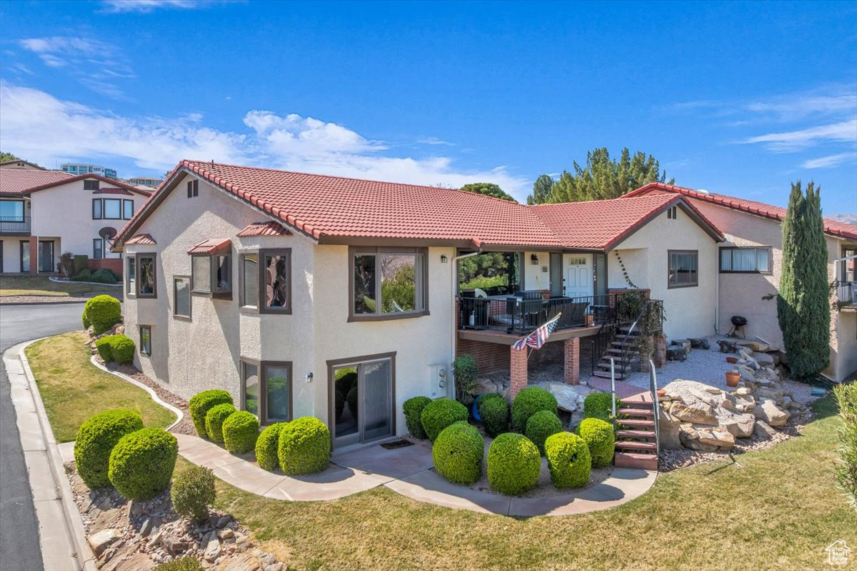 View of front of house with stucco siding, stairway, a front yard, and a tiled roof