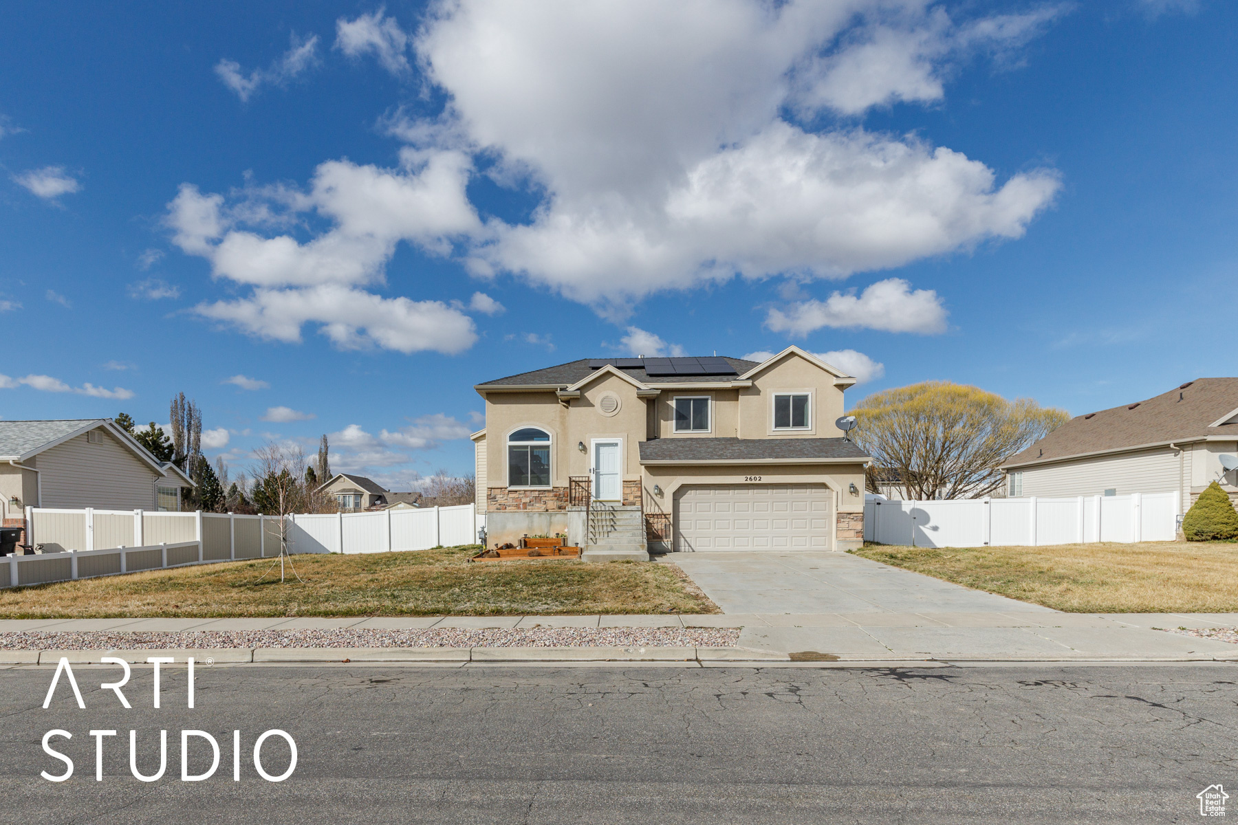 View of front of property with solar panels, concrete driveway, a front yard, and fence