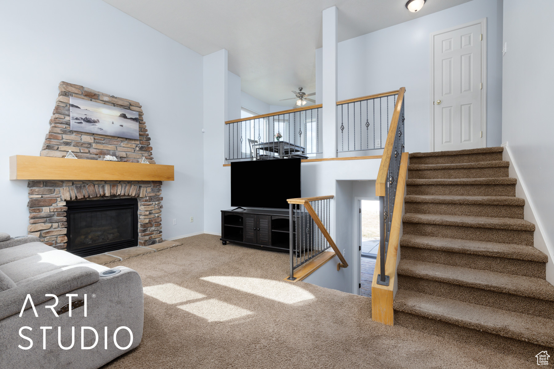 Living area with baseboards, stairs, carpet flooring, a stone fireplace, and a ceiling fan