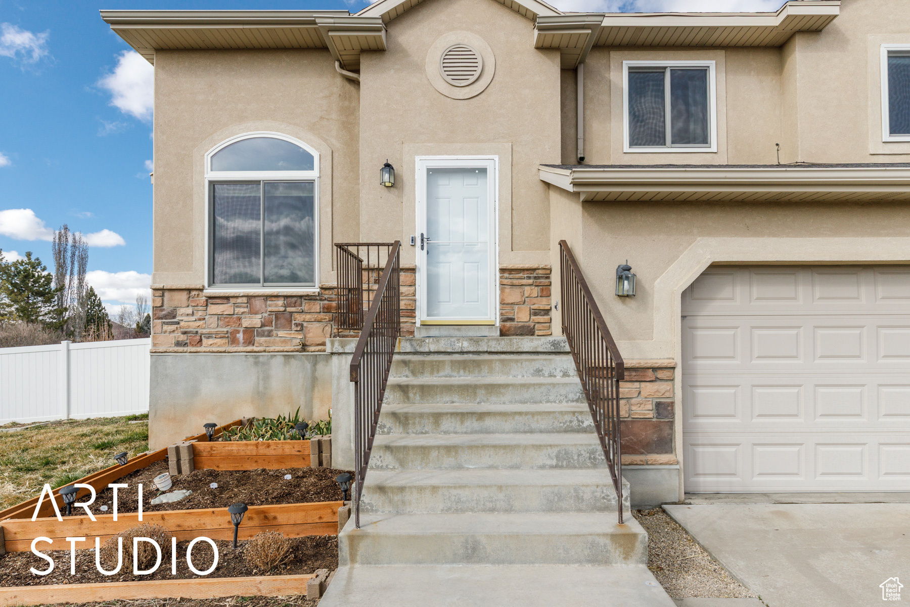 View of front facade featuring stone siding, stucco siding, an attached garage, and fence