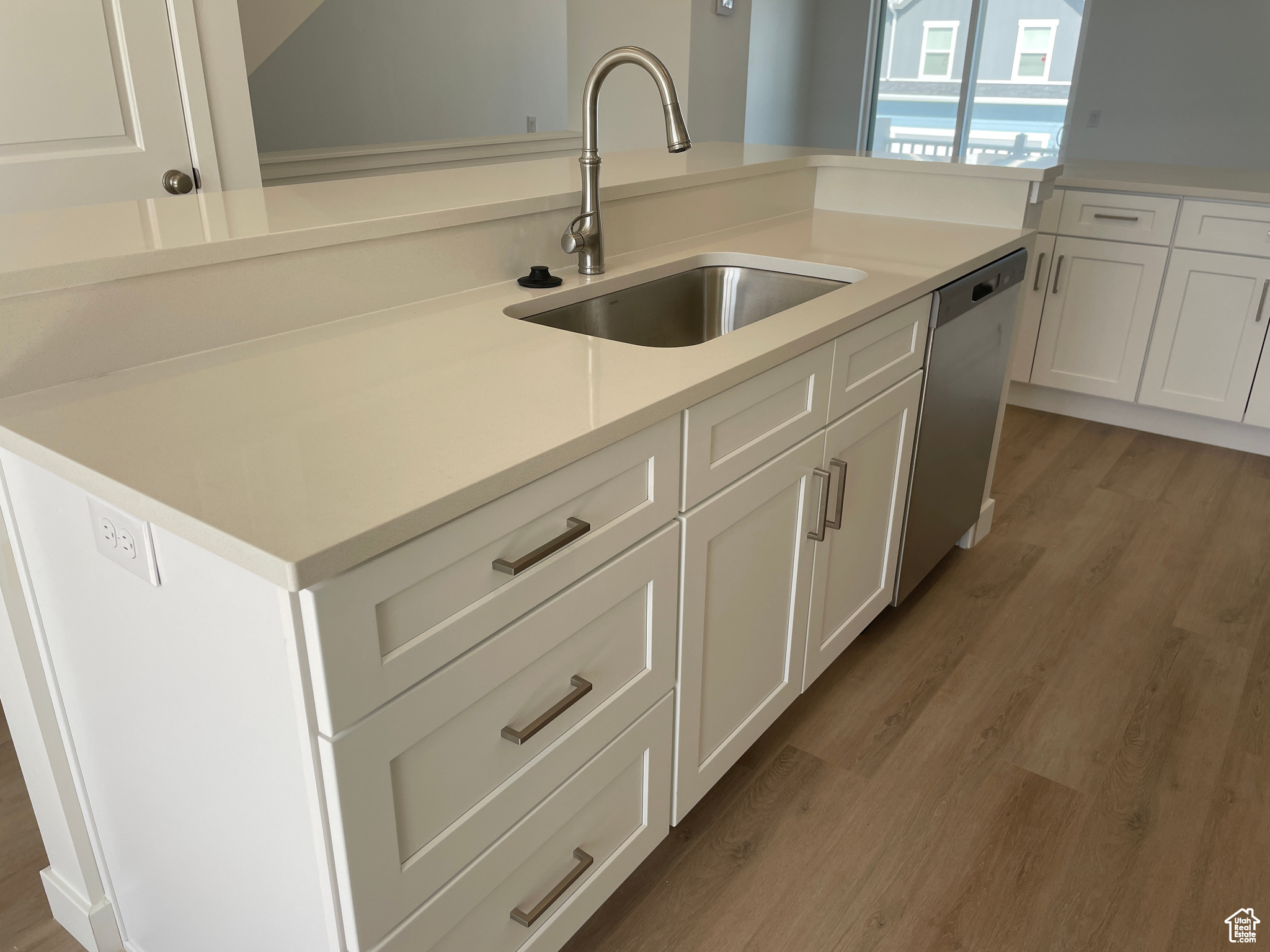 Kitchen featuring a sink, stainless steel dishwasher, white cabinetry, light wood-style floors, and light countertops