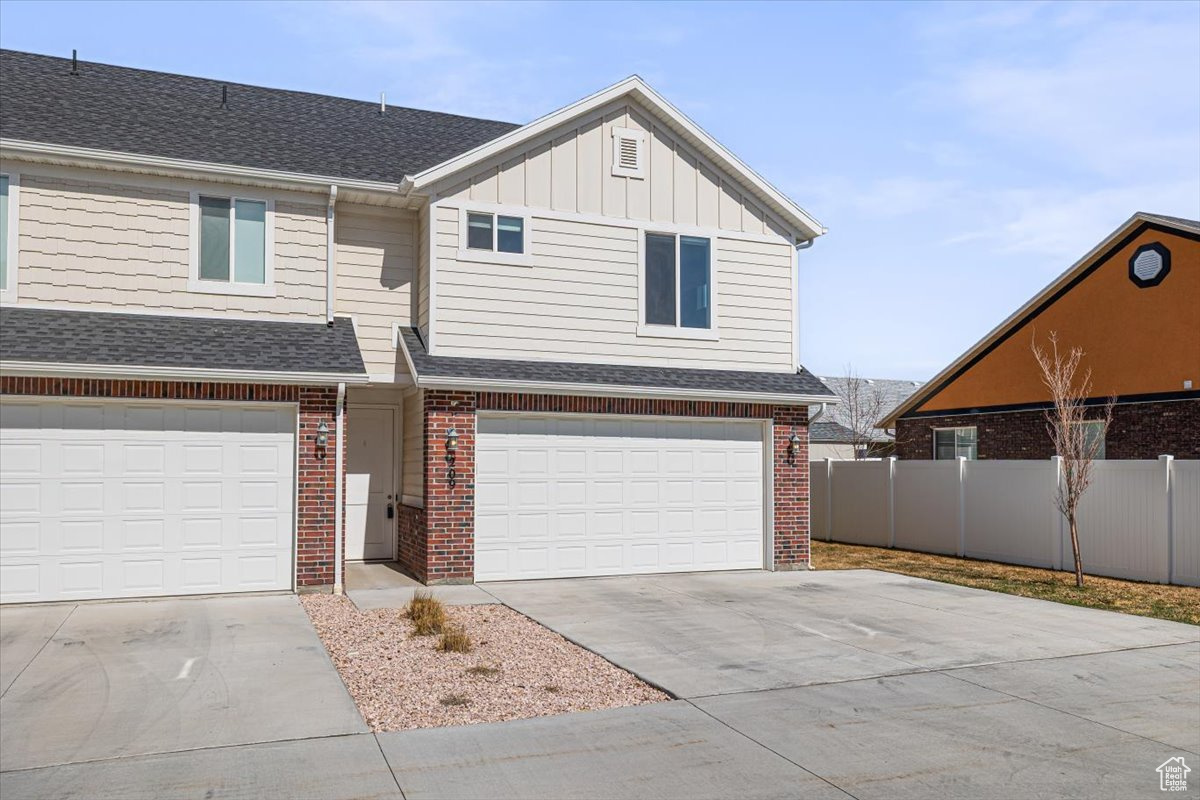 View of front of property with brick siding, board and batten siding, driveway, and fence