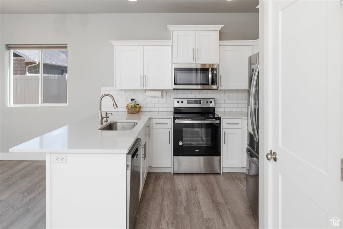 Kitchen featuring light wood-style flooring, a sink, backsplash, stainless steel appliances, and a peninsula