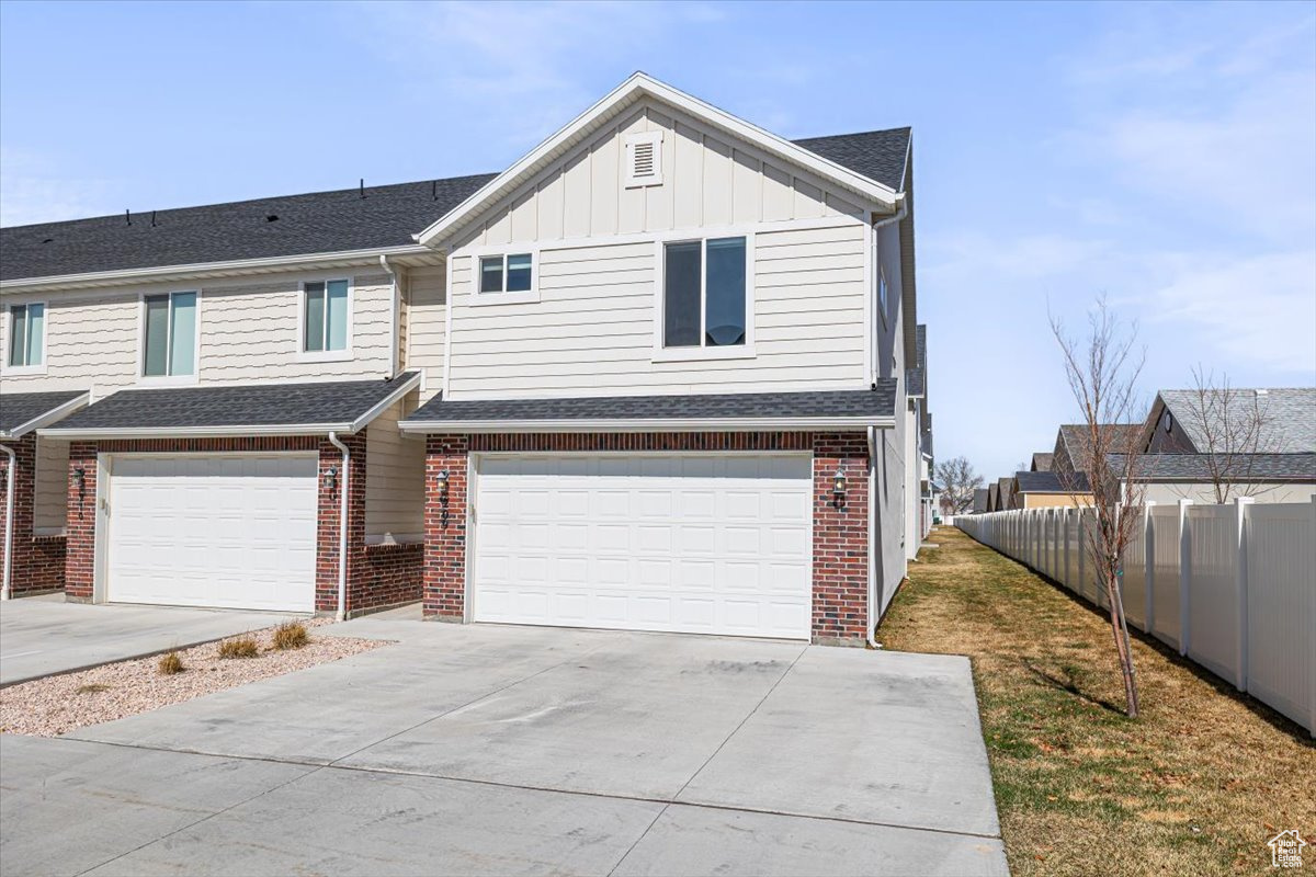 View of front facade featuring fence, driveway, a garage, board and batten siding, and brick siding