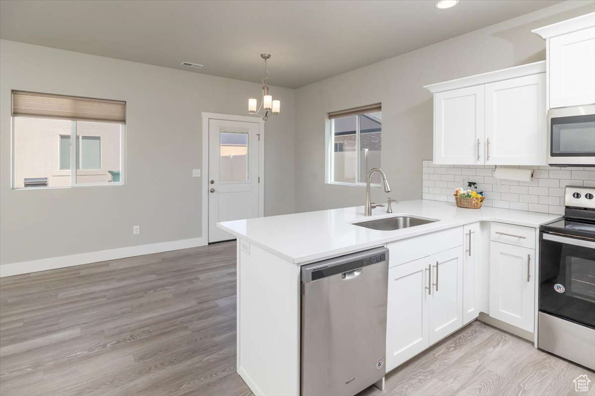 Kitchen featuring a sink, appliances with stainless steel finishes, a peninsula, light countertops, and decorative backsplash