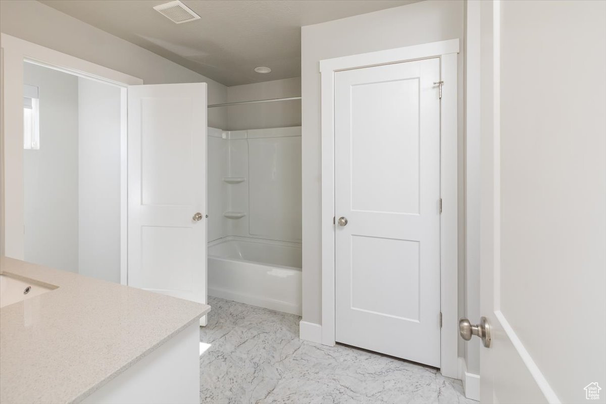 Full bath featuring visible vents, vanity, marble finish floor, and washtub / shower combination