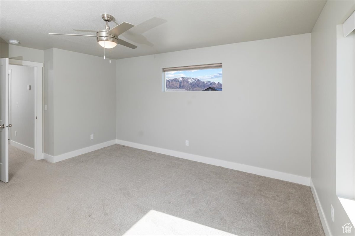 Empty room with a ceiling fan, baseboards, and light carpet