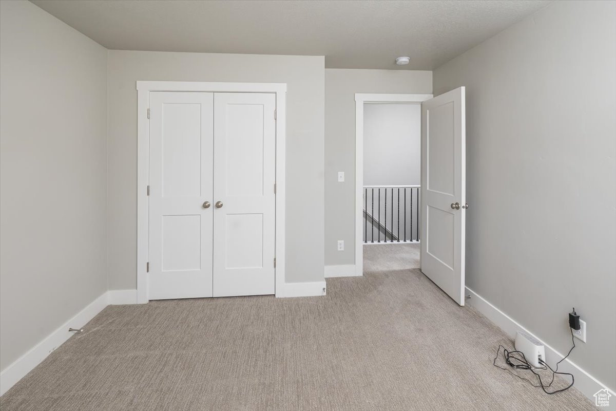 Unfurnished bedroom with a closet, light colored carpet, and baseboards