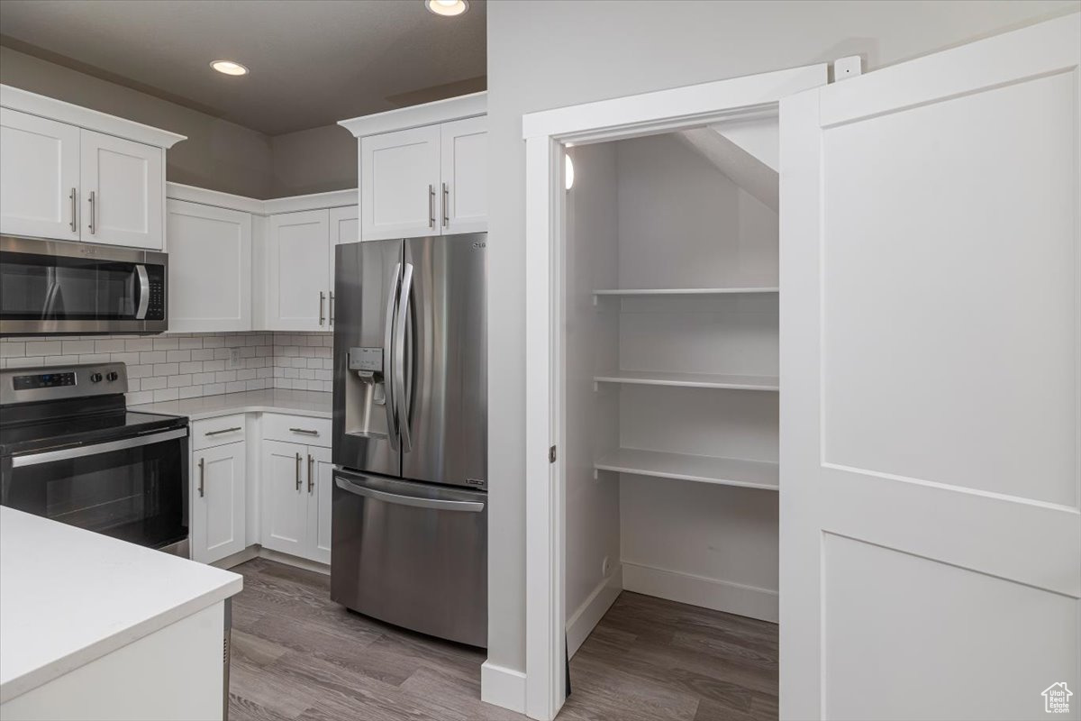 Kitchen featuring backsplash, white cabinets, stainless steel appliances, and light countertops