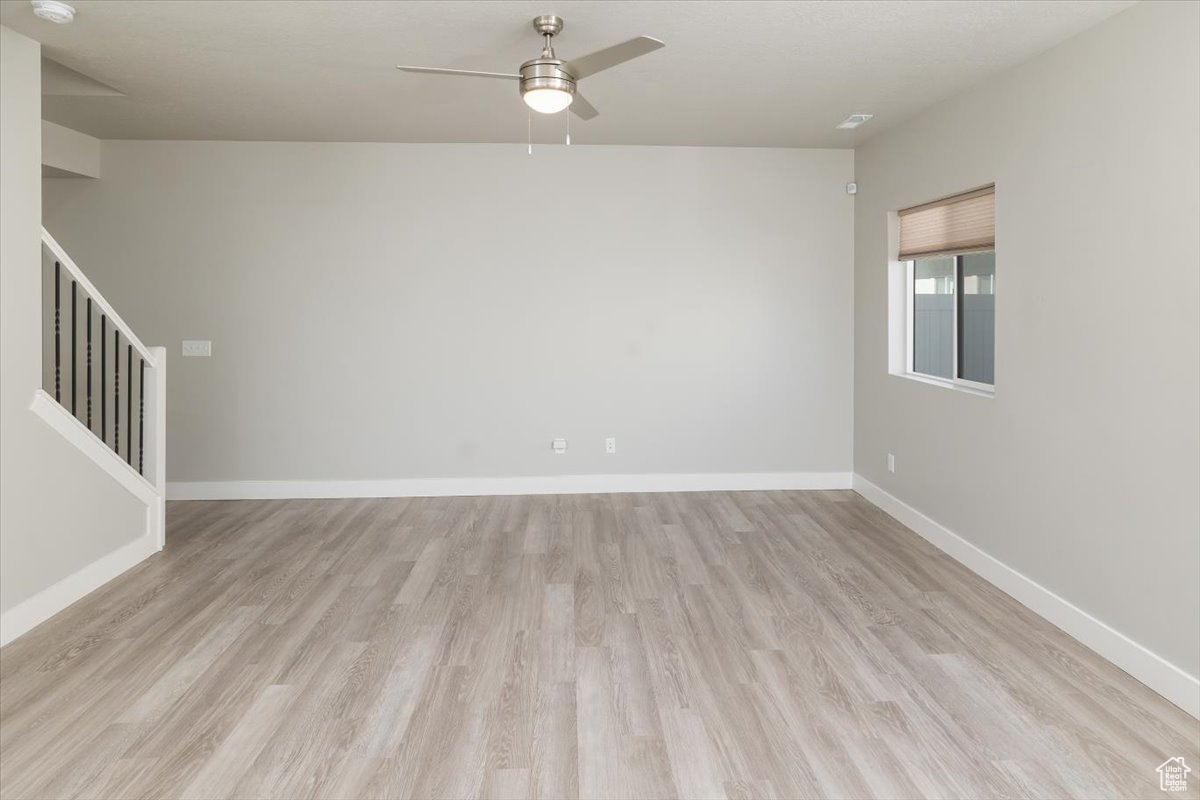 Spare room featuring stairway, a ceiling fan, light wood-type flooring, and baseboards