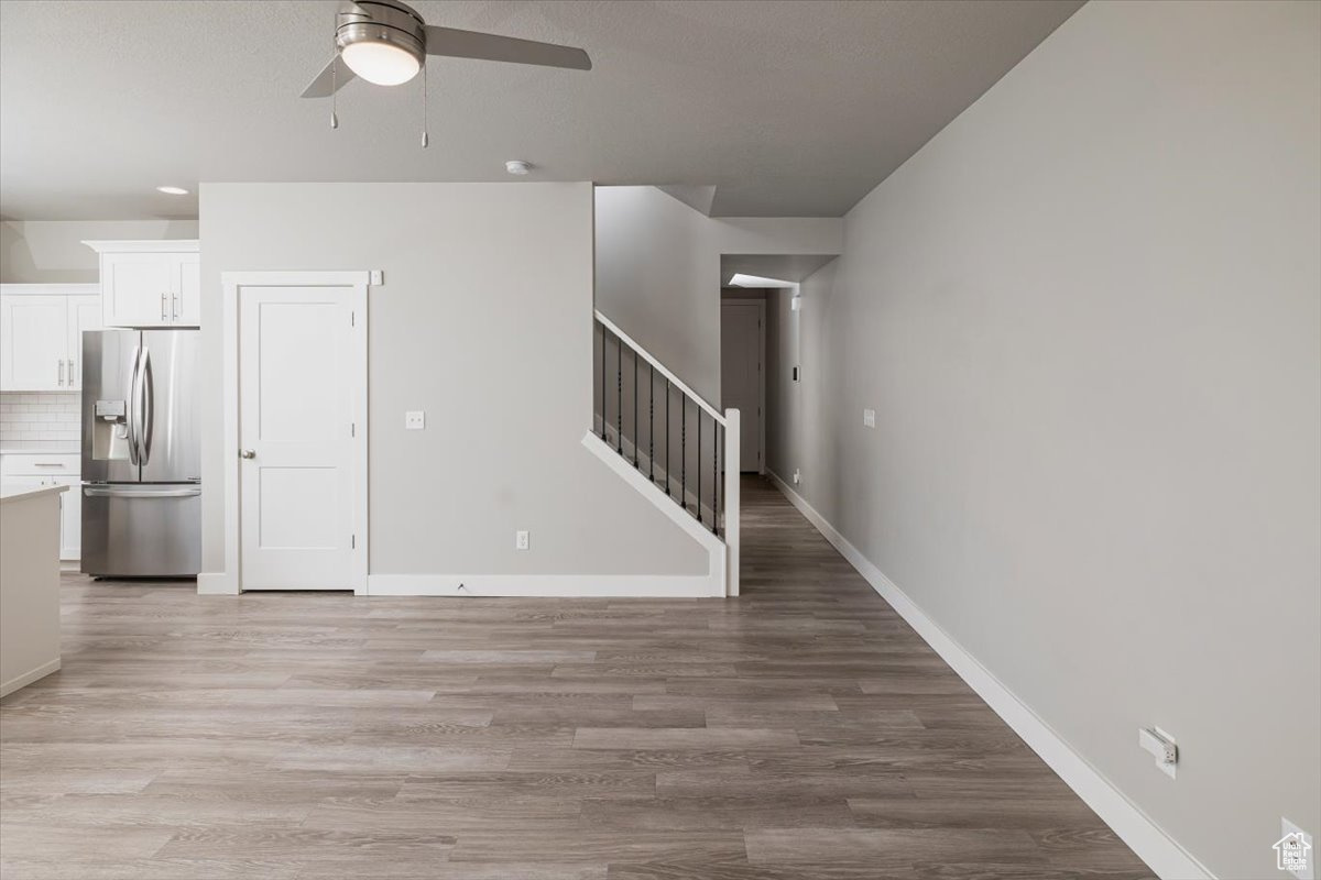 Unfurnished living room featuring baseboards, a ceiling fan, stairs, and light wood finished floors