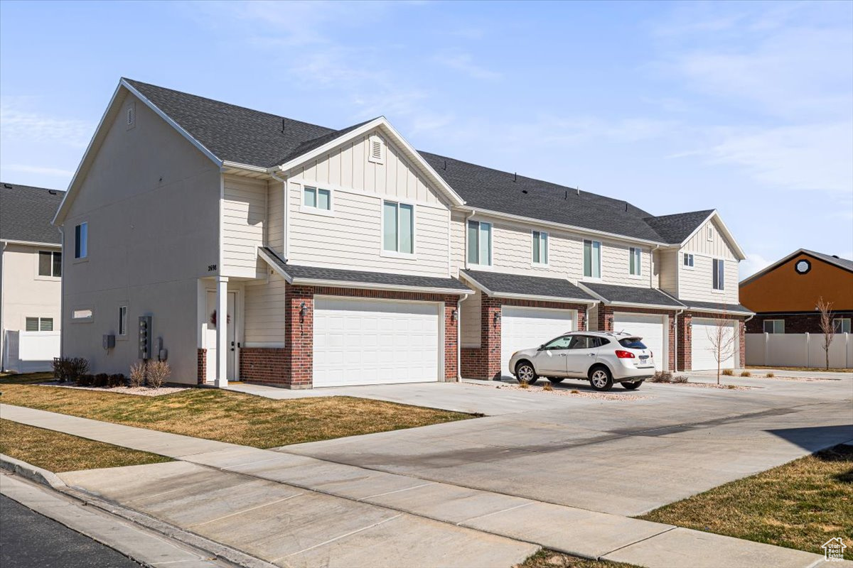 Multi unit property featuring brick siding, board and batten siding, driveway, and a garage