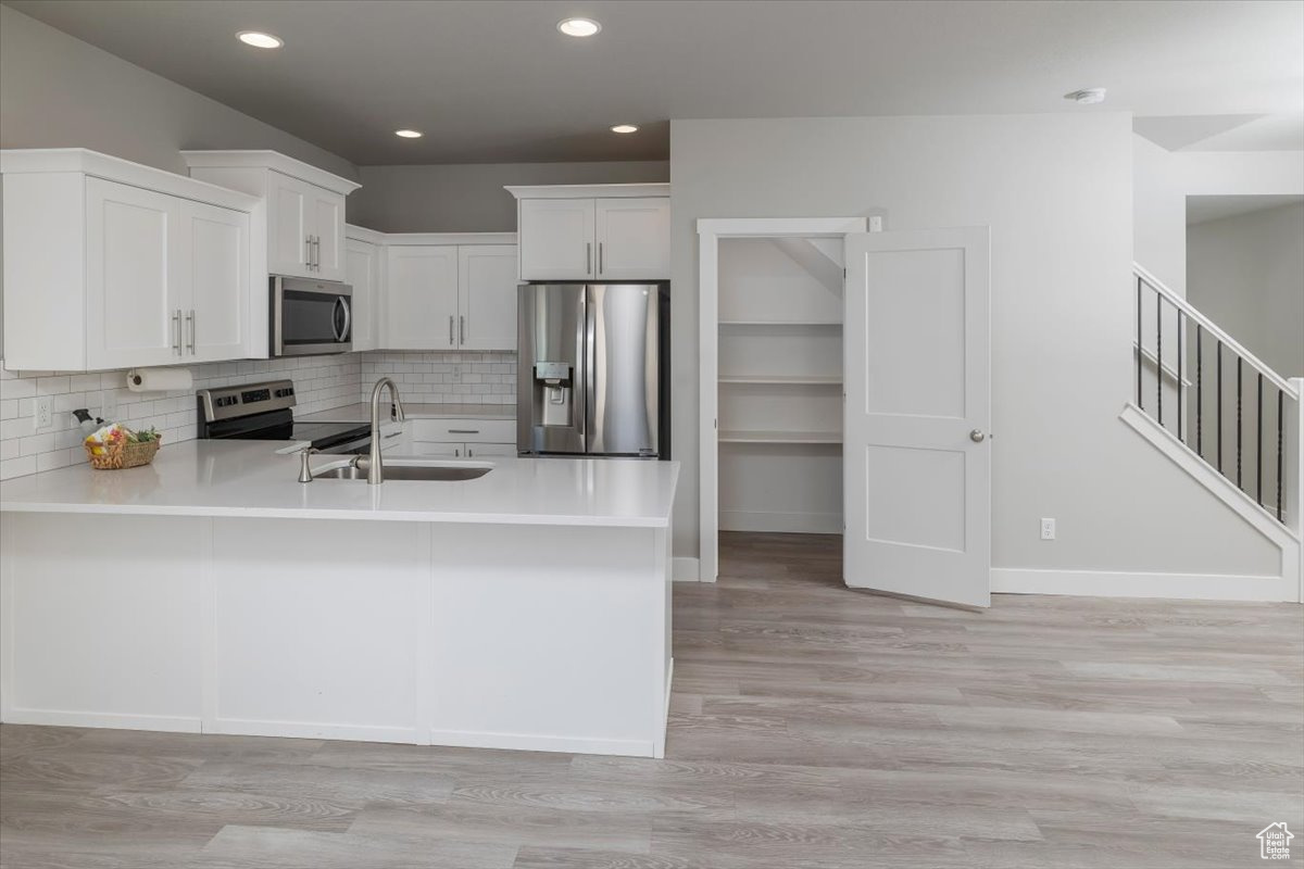 Kitchen with appliances with stainless steel finishes, light countertops, a peninsula, and a sink