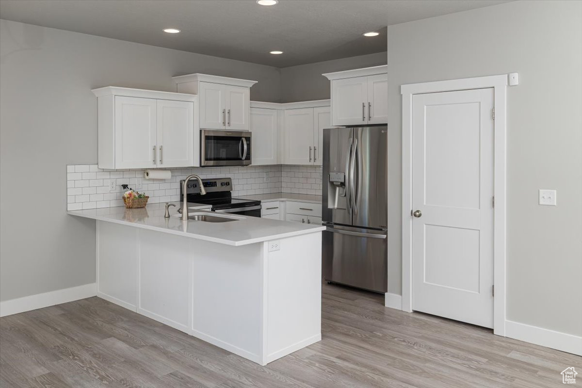 Kitchen featuring tasteful backsplash, light wood-style flooring, appliances with stainless steel finishes, a peninsula, and a sink