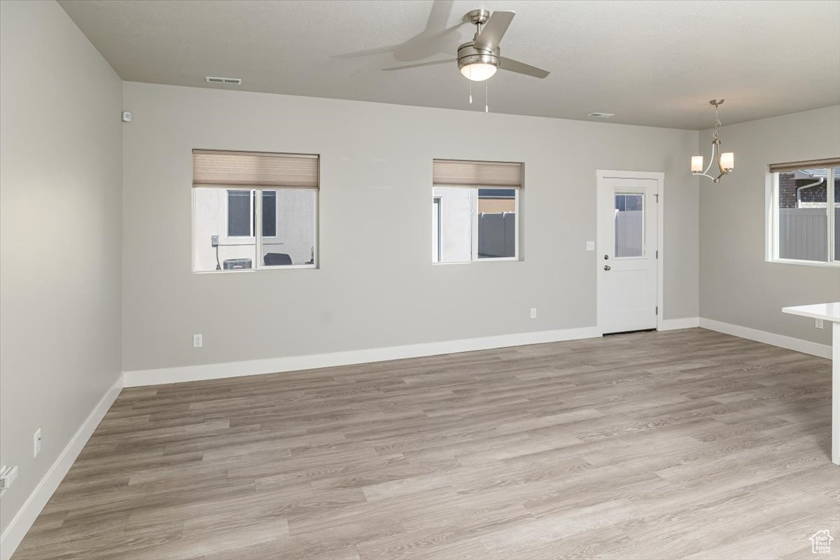 Spare room with visible vents, baseboards, light wood-style floors, and ceiling fan with notable chandelier