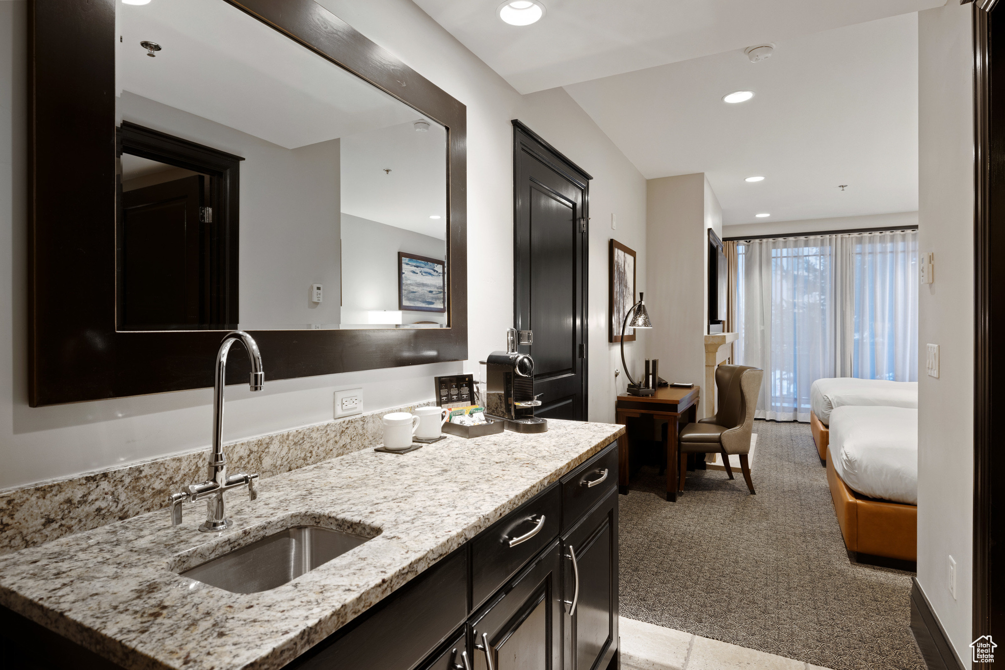 Kitchen featuring dark cabinetry, light stone countertops, recessed lighting, a sink, and light carpet