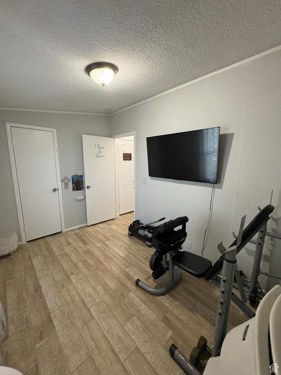 Exercise area featuring ornamental molding, wood finished floors, and a textured ceiling