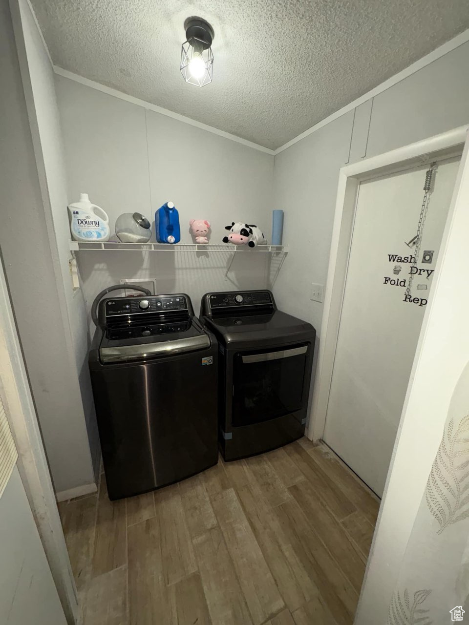 Laundry room with a textured ceiling, wood finished floors, crown molding, laundry area, and washing machine and clothes dryer