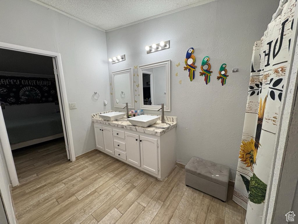 Ensuite bathroom with a sink, a textured ceiling, wood finished floors, and double vanity