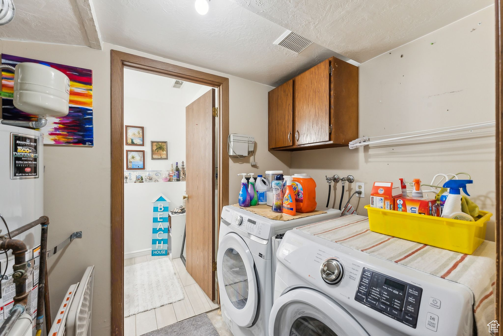 Clothes washing area with washing machine and clothes dryer, visible vents, cabinet space, and a textured ceiling