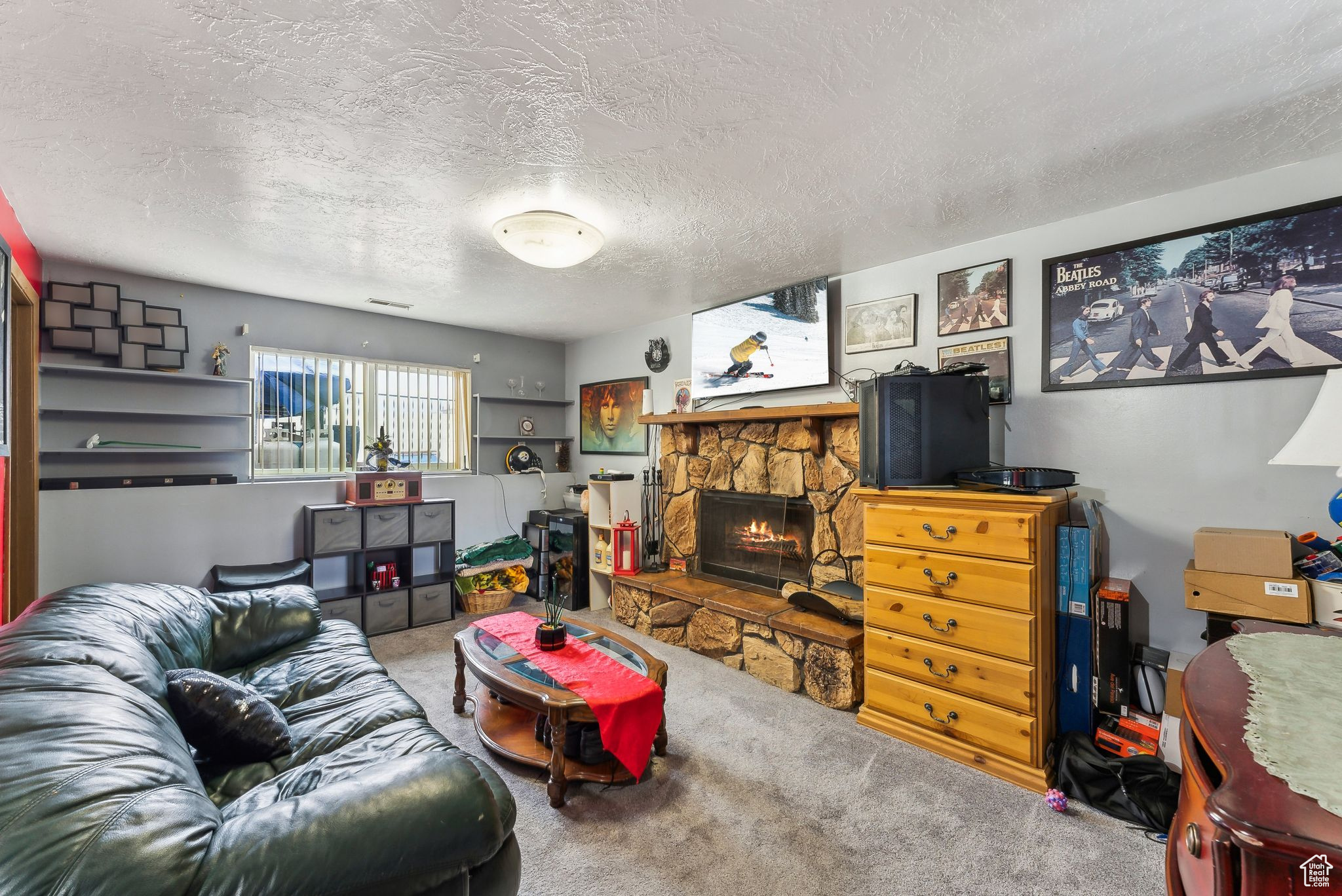 Living room with a stone fireplace, carpet floors, textured ceilings, and has a crawl space with extra storage