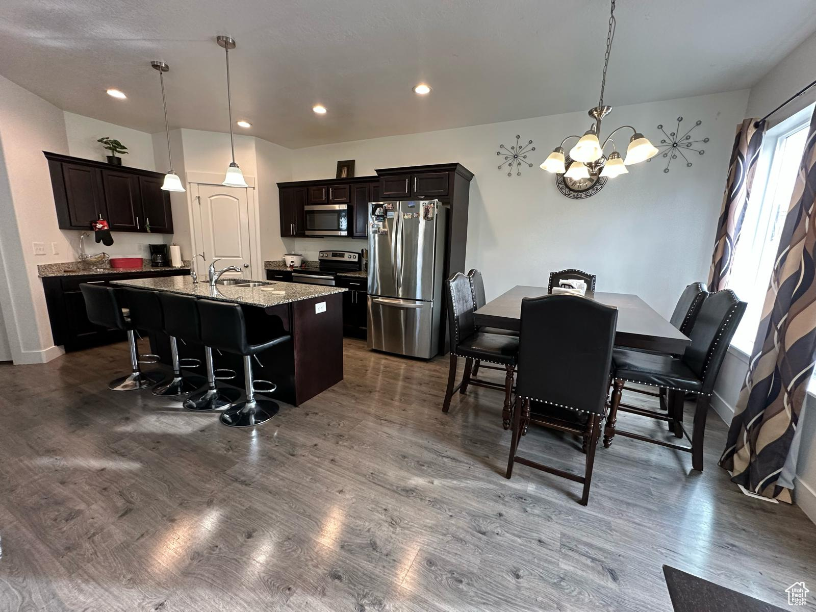 Kitchen with a breakfast bar, dark wood-style floors, a kitchen island with sink, and stainless steel appliances