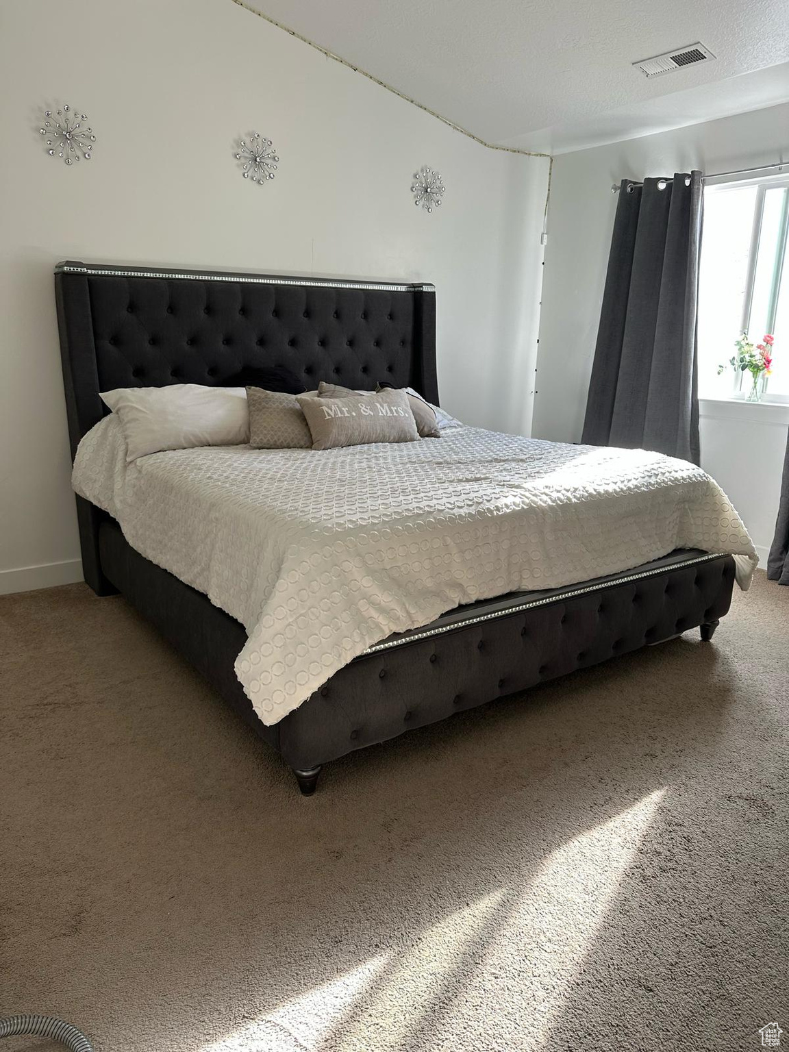 Carpeted bedroom with lofted ceiling, visible vents, and baseboards