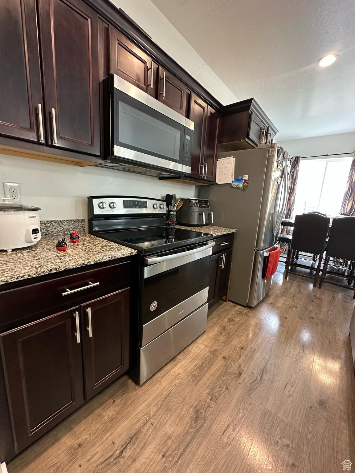 Kitchen featuring stainless steel appliances, light wood-type flooring, dark brown cabinetry, and light stone countertops
