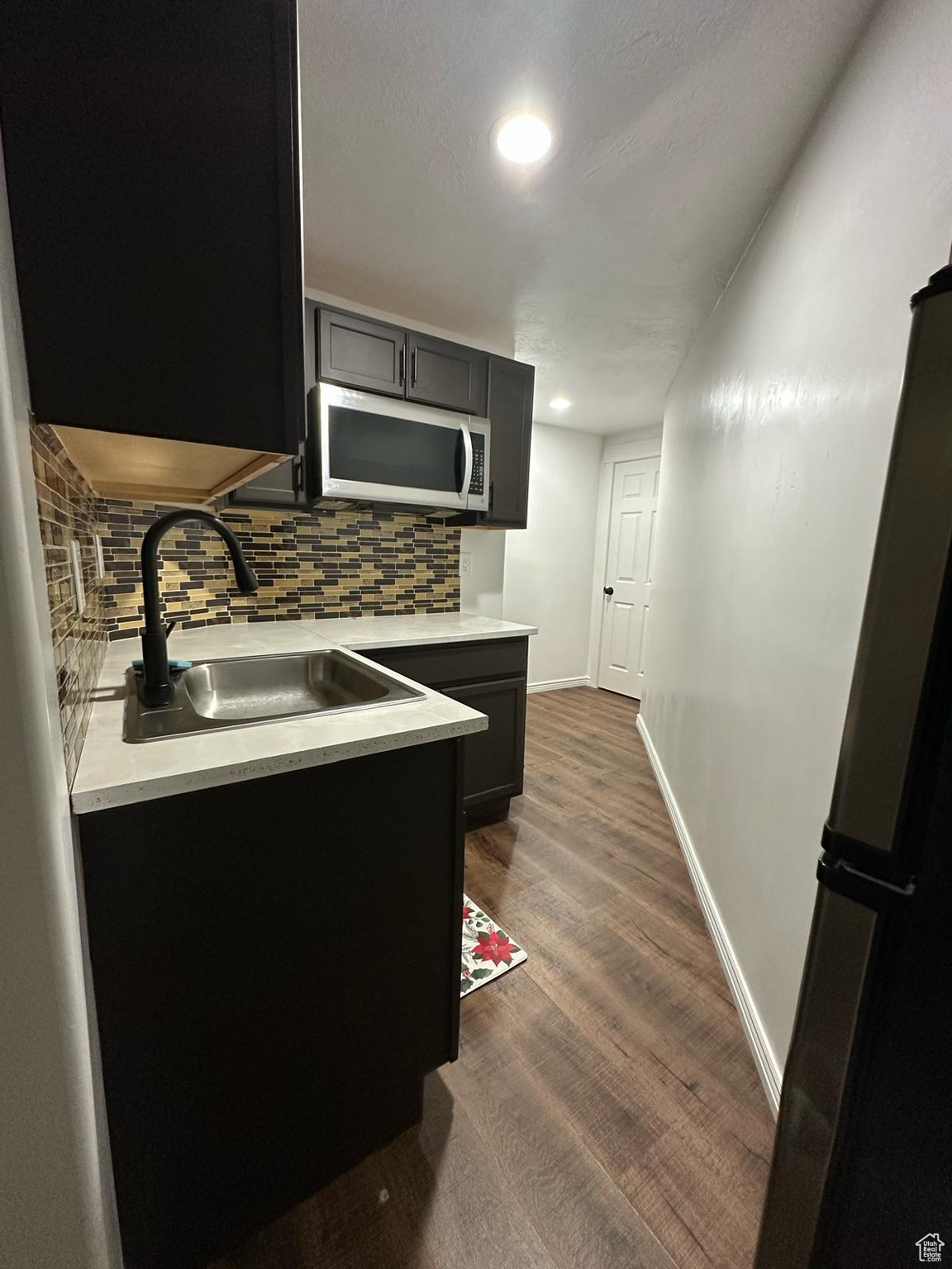 Kitchen with light countertops, stainless steel microwave, a sink, and backsplash