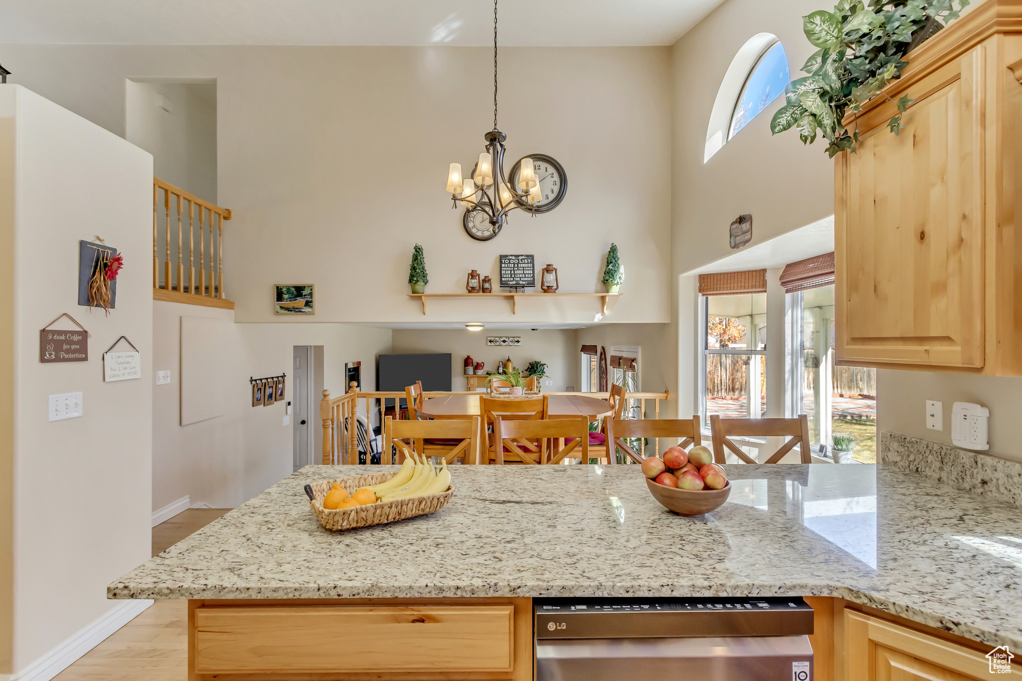 Kitchen featuring light brown cabinetry, a chandelier, a towering ceiling, and light stone countertops