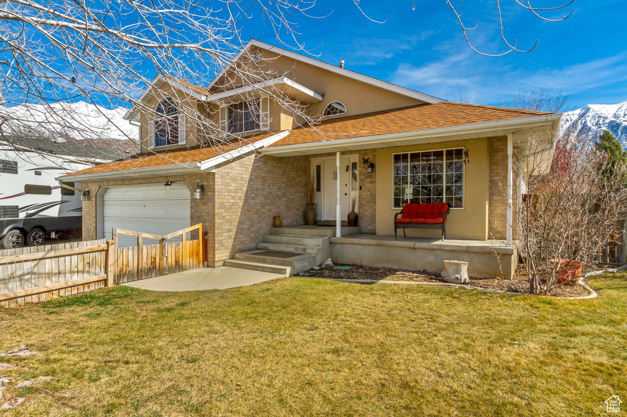 View of front of house featuring brick siding, a shingled roof, fence, a front yard, and covered porch
