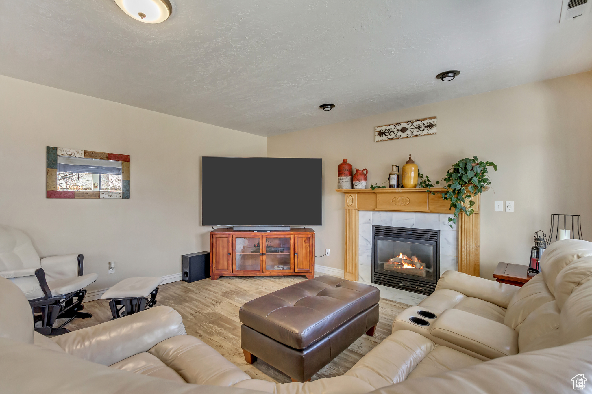 Living room featuring a tiled fireplace, light wood-style floors, visible vents, and baseboards