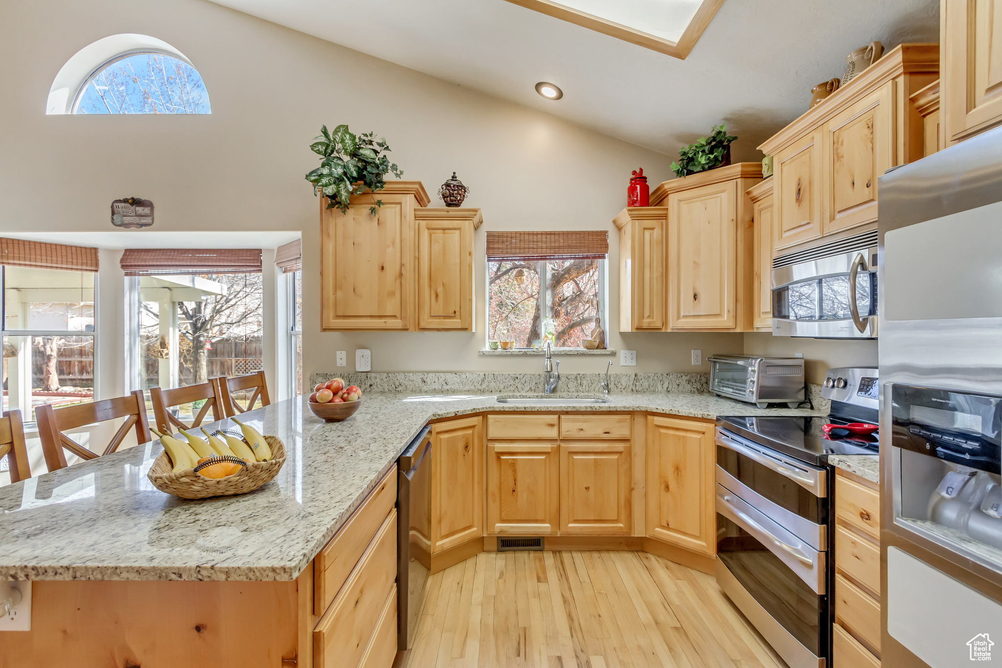 Kitchen with light brown cabinetry, a sink, stainless steel appliances, a peninsula, and lofted ceiling