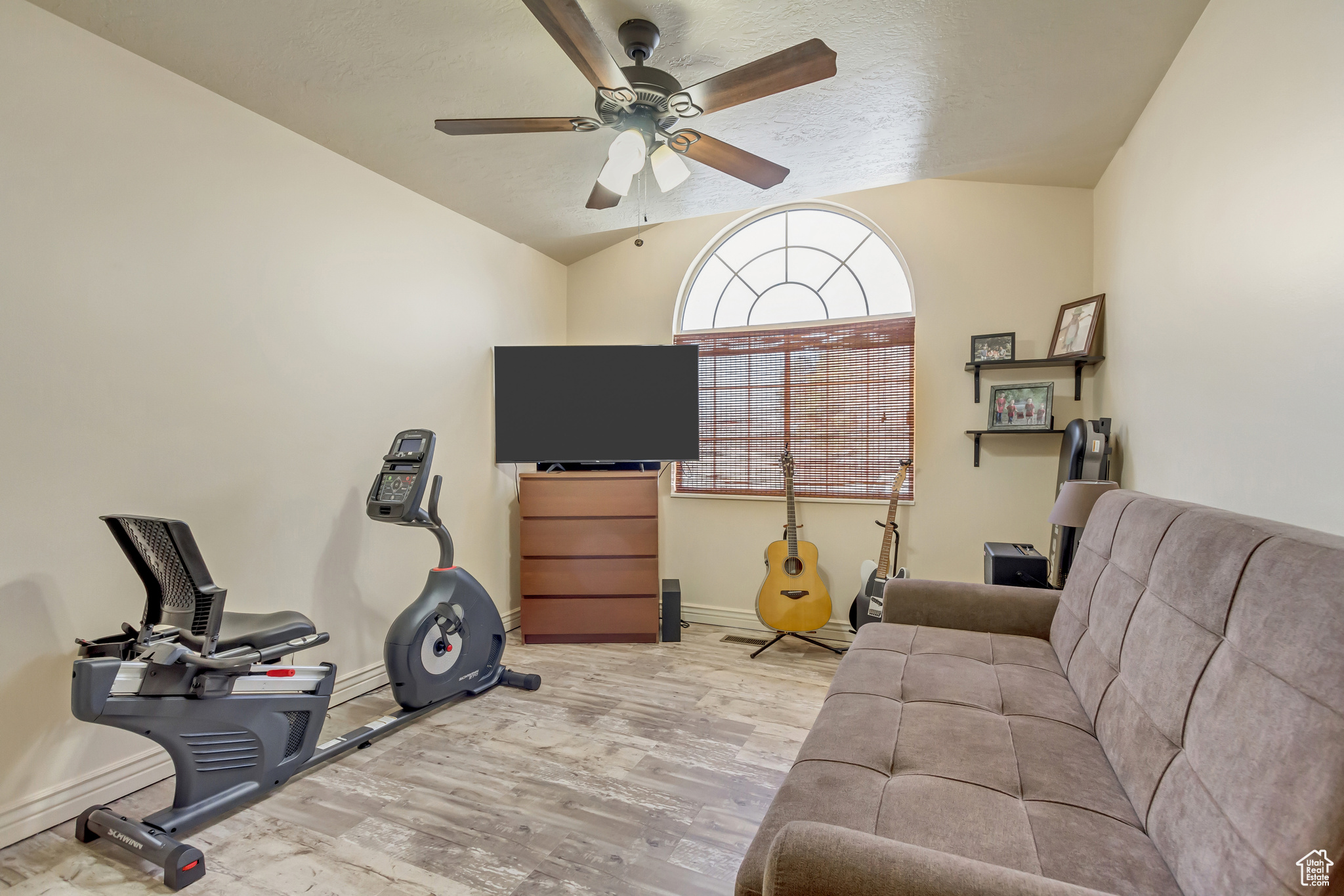Living room featuring a ceiling fan, wood finished floors, baseboards, vaulted ceiling, and a textured ceiling