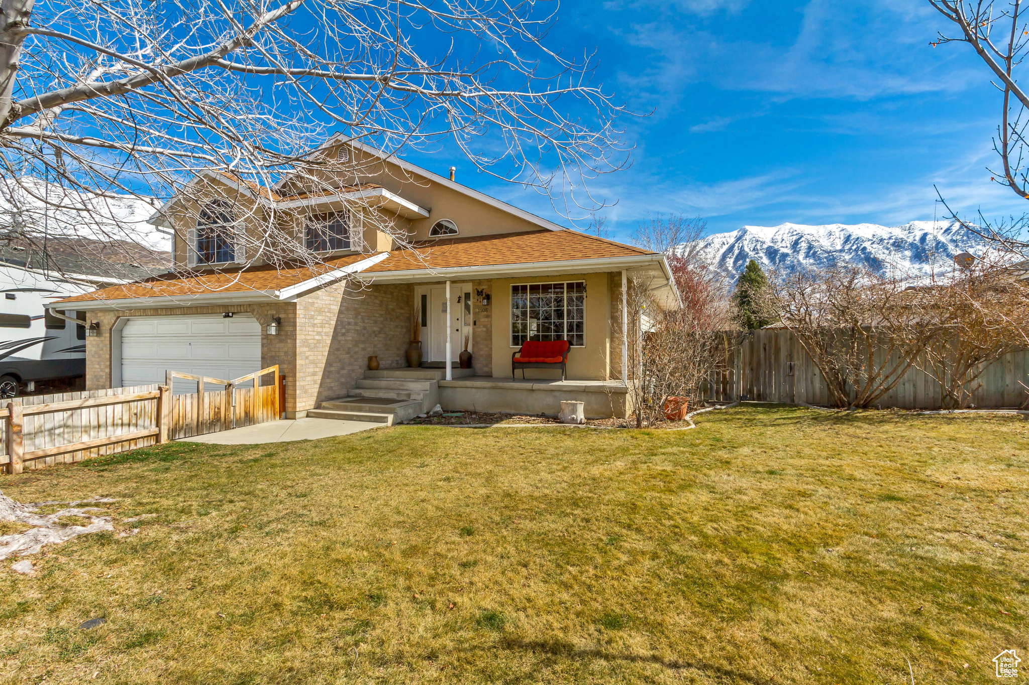View of front of home with fence, a porch, brick siding, a front lawn, and a mountain view