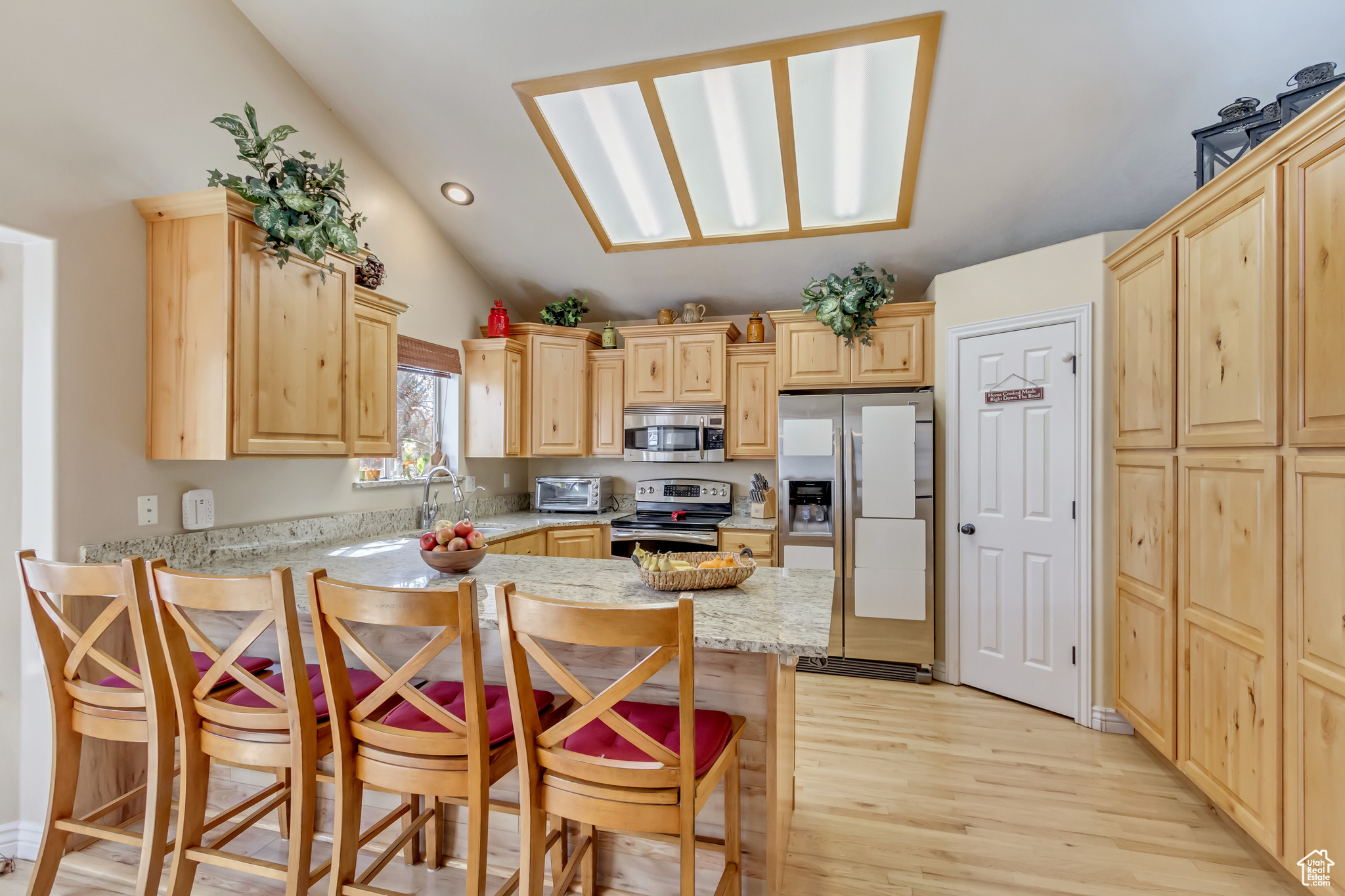 Kitchen featuring a kitchen bar, lofted ceiling with skylight, light brown cabinets, appliances with stainless steel finishes, and light stone countertops