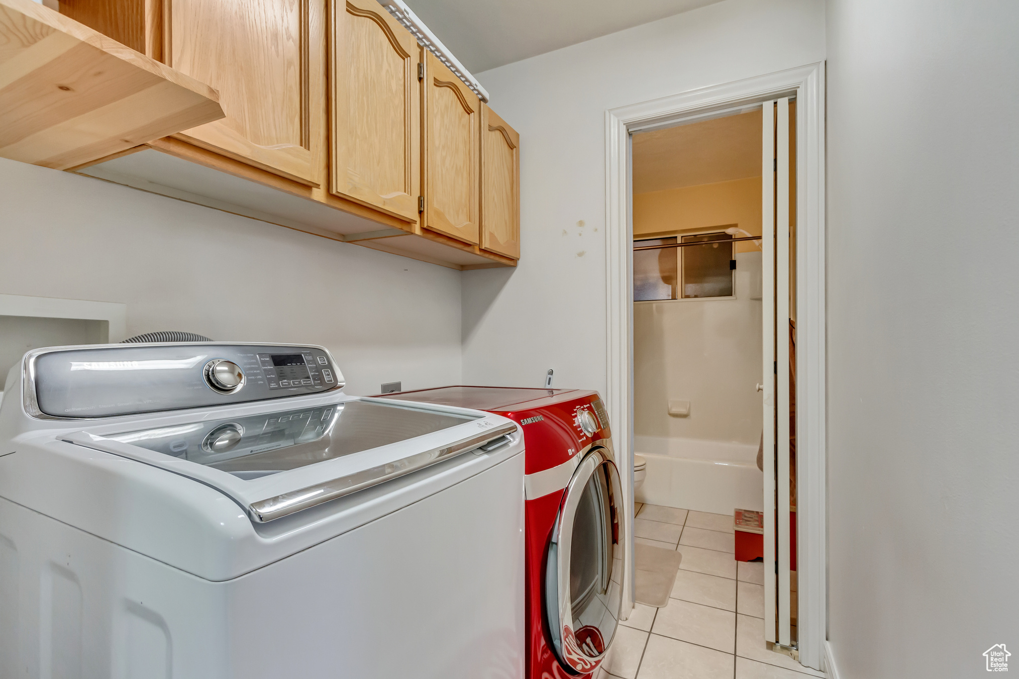 Washroom featuring light tile patterned flooring, cabinet space, and washing machine and clothes dryer