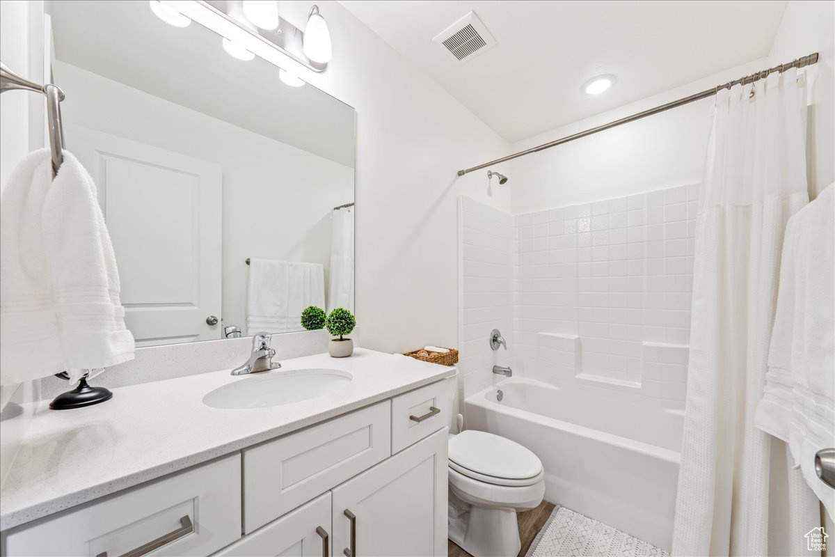 Full bathroom featuring vanity, toilet, shower / bathtub combination with curtain, and visible vents