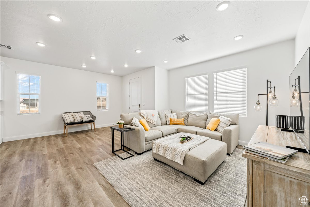 Living room featuring light wood finished floors, visible vents, recessed lighting, and a wealth of natural light