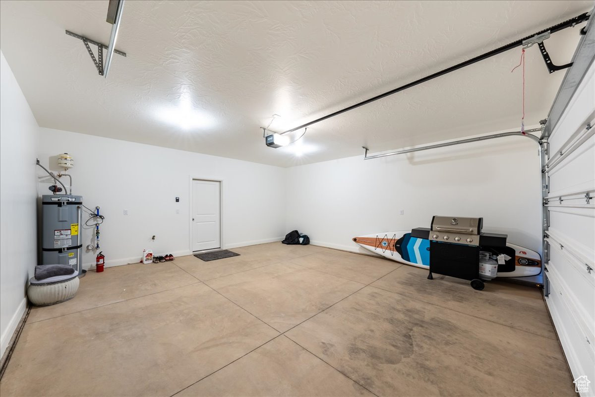 Garage featuring baseboards, a garage door opener, and water heater
