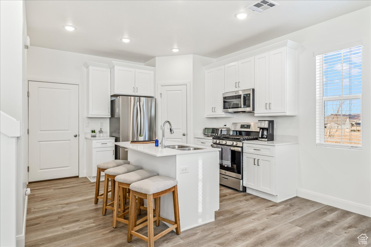 Kitchen with visible vents, a sink, stainless steel appliances, light wood-style floors, and a kitchen bar