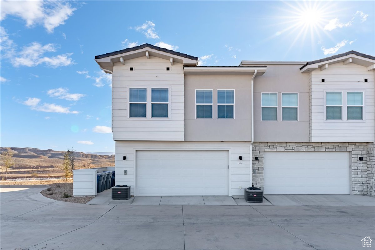 Exterior space featuring stone siding, stucco siding, central air condition unit, and a garage