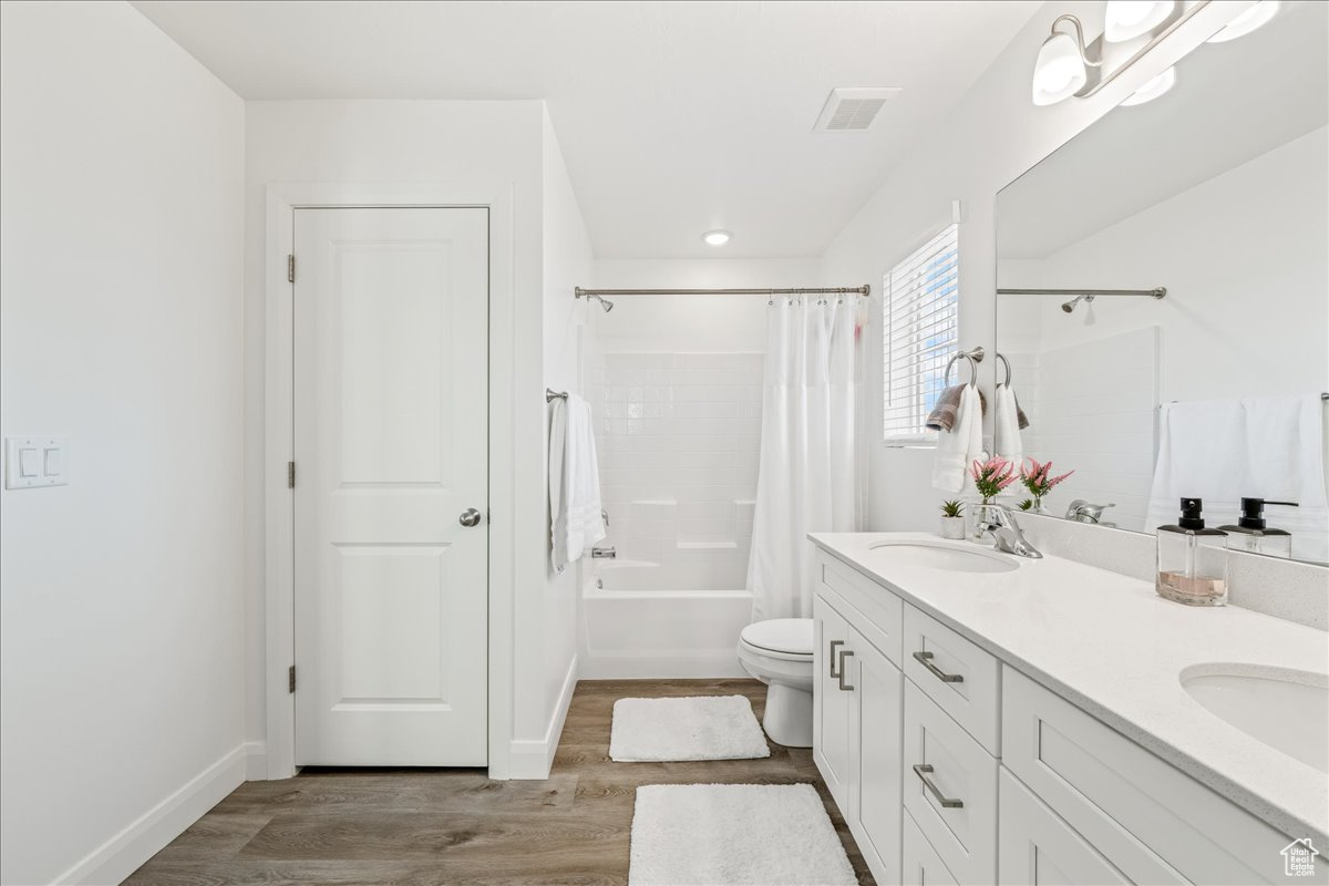 Bathroom featuring visible vents, toilet, double vanity, wood finished floors, and a sink